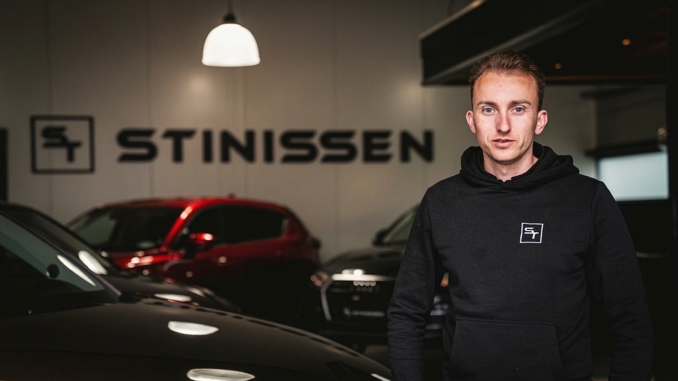 Jermain Stinissen in zijn showroom, naast een donkere occasion onder het logo van Stinissen Auto's